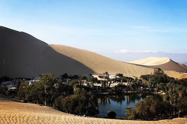 Ica Valley Peru travel guide - golden sand dunes surrounding Huacachina oasis under sunset sky